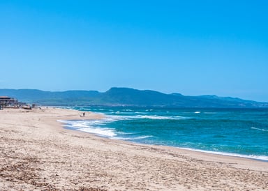 Badesi Kitesurfing in Sardinia image of a lonely sandy beach with blue sky and Mountains in the background