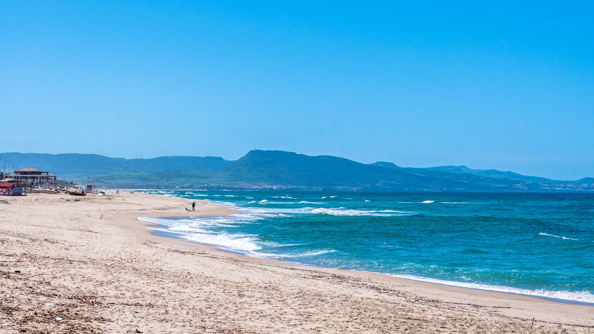 Badesi Kitesurfing in Sardinia image of a lonely sandy beach with blue sky and Mountains in the background