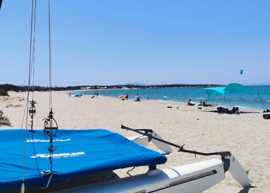 Paralia Glifada Kitesurfing in Naxos Greece with a catamaran boat in front on white sand, some people laying on the beach and a few kitesurfers surfing in the background