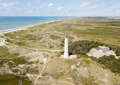 Hvide Sand Kiteboarding at Denmark coastline with lighthouse in front, green open fields and blue sea in the background