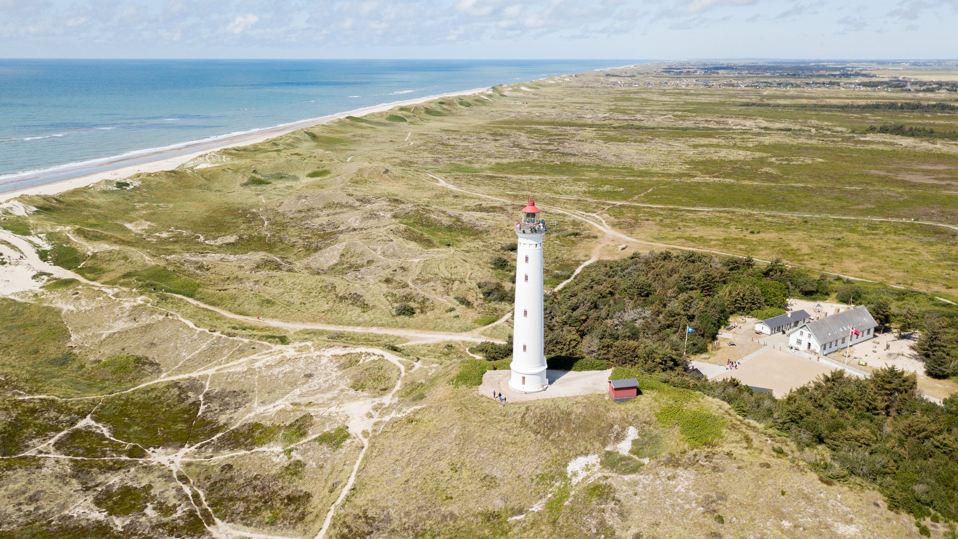 Hvide Sand Kiteboarding at Denmark coastline with lighthouse in front, green open fields and blue sea in the background