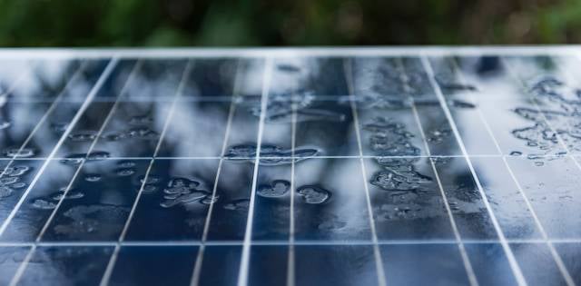 Solar panels mounted on the ground are covered with raindrops and absorb minimal sunlight during a storm.