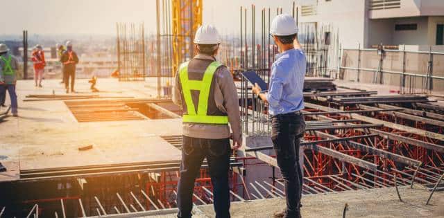 Two construction workers stand on a structure they are building to discuss how to make it more durable and resilient.