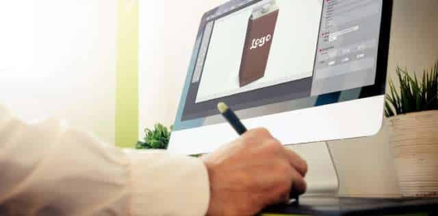 A person is working on a computer designing a package for a product. The mock-up says "logo" on a brown carton.