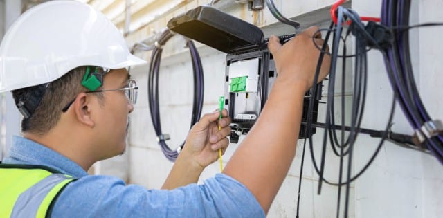 An engineer installing fiber optic internet to a building's exterior. He is connecting cables to the hang wires.