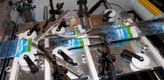 An industrial machine prints and cuts shrink sleeves for packaging, with a belt carrying uncut sleeves.