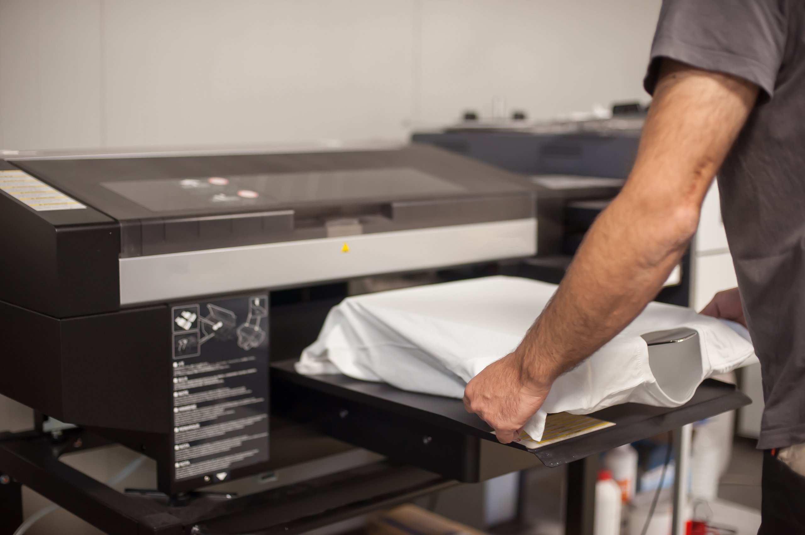A graphic technician putting a blank, white t-shirt into a direct-to-film printer to transfer a graphic onto it.