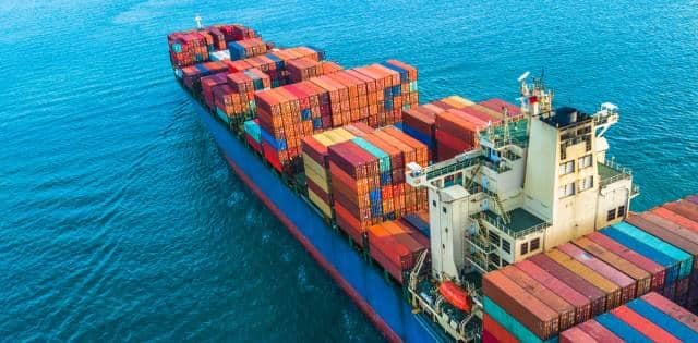 A large carrier ship sailing at sea covered with stacks of hundreds of multicolored shipping containers.