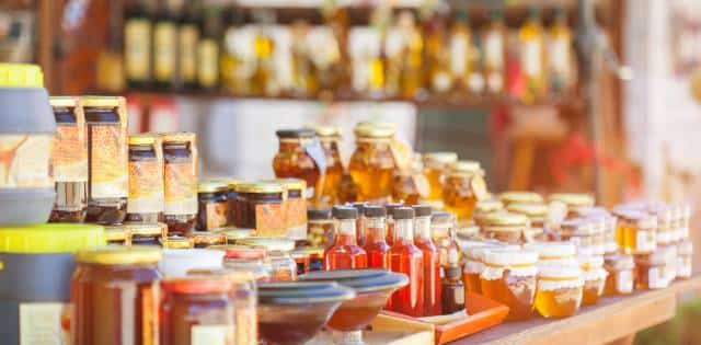 A display table with several sizes and varieties of honey jars with a shelf of more honey products in the background.