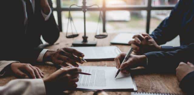 Four people sit at a table in a law office. They are making notes and discussing the contract in front of them.