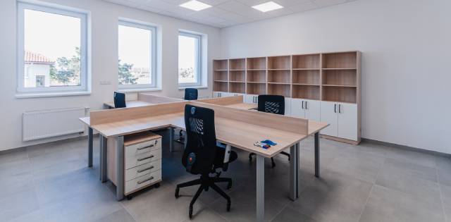 Office furniture, including desk space and swivel chairs for four employees, sitting in a small plain white room.