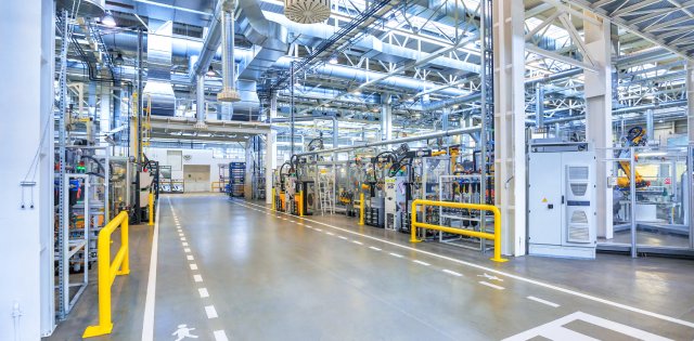 The interior of an industrial manufacturing facility with a long corridor with side walking paths and yellow railings.