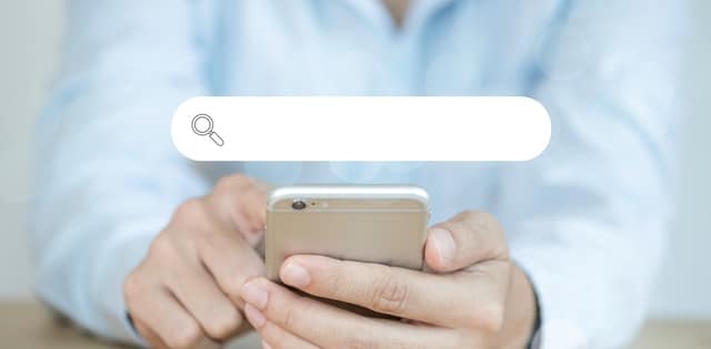 A business owner sitting down at a table with their cell phone in their hands. There's a browser graphic over the phone.