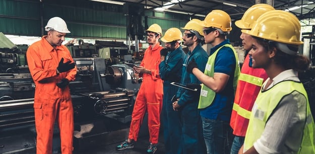 Several people standing together in an industrial facility while wearing safety gear like hard hats and high-visibility garments.