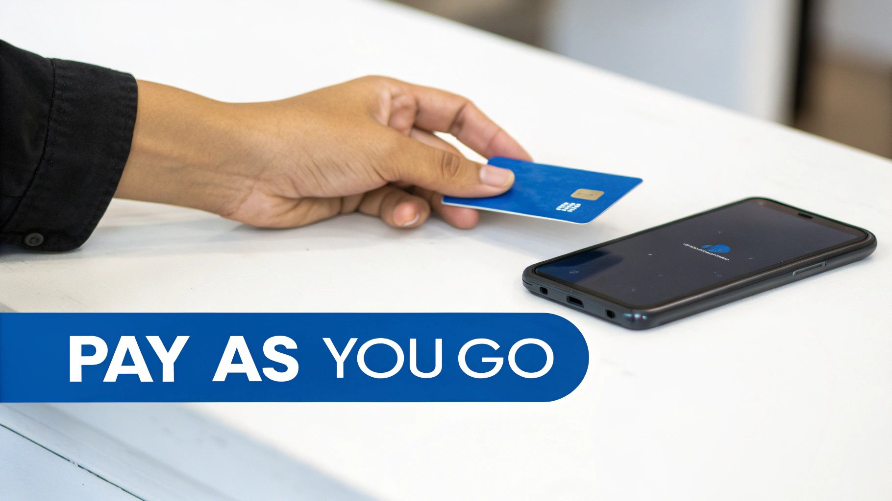 Une main tient une carte bleue près d'un smartphone sur une table blanche, avec le texte 'PAY AS YOU GO'.