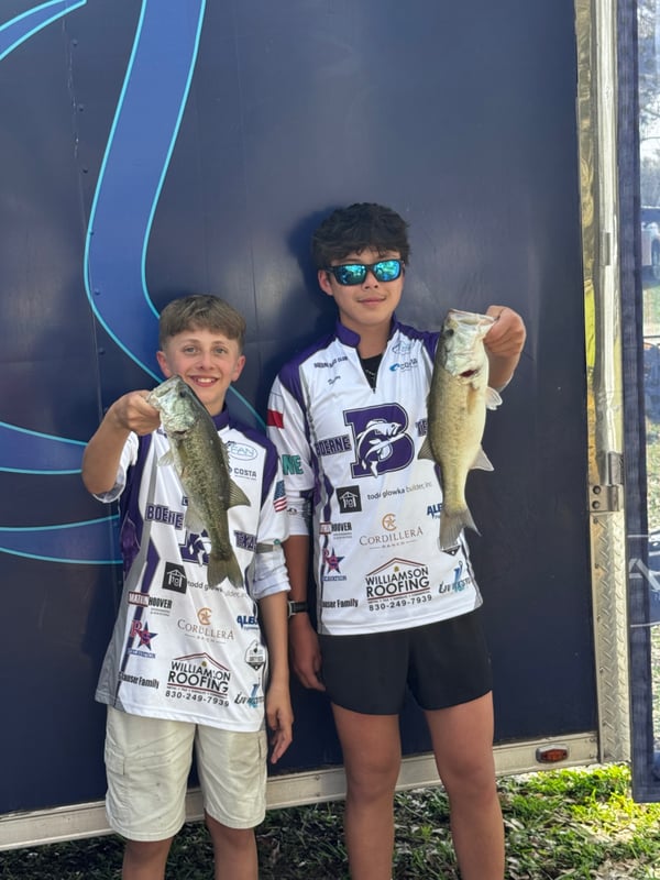 Two young anglers proudly holding their caught bass at a tournament