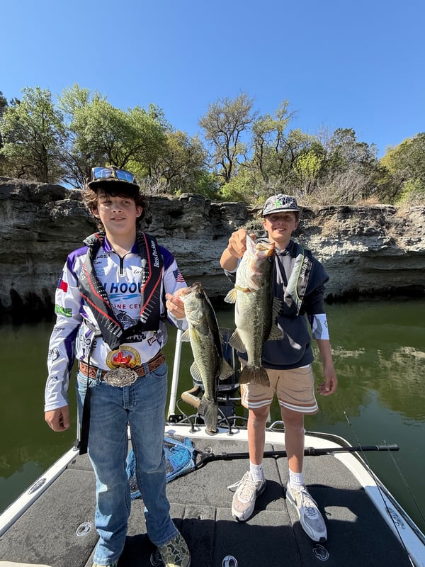 Two young anglers proudly holding their bass catch on a boat