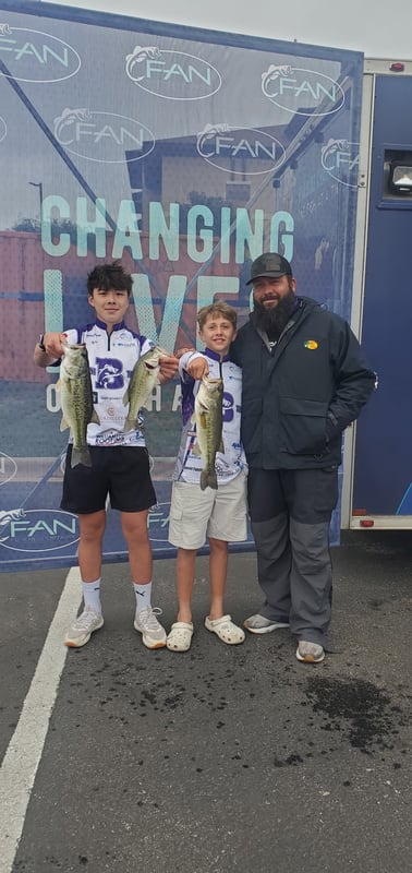 Two young anglers proudly display their bass catches at a fishing tournament.