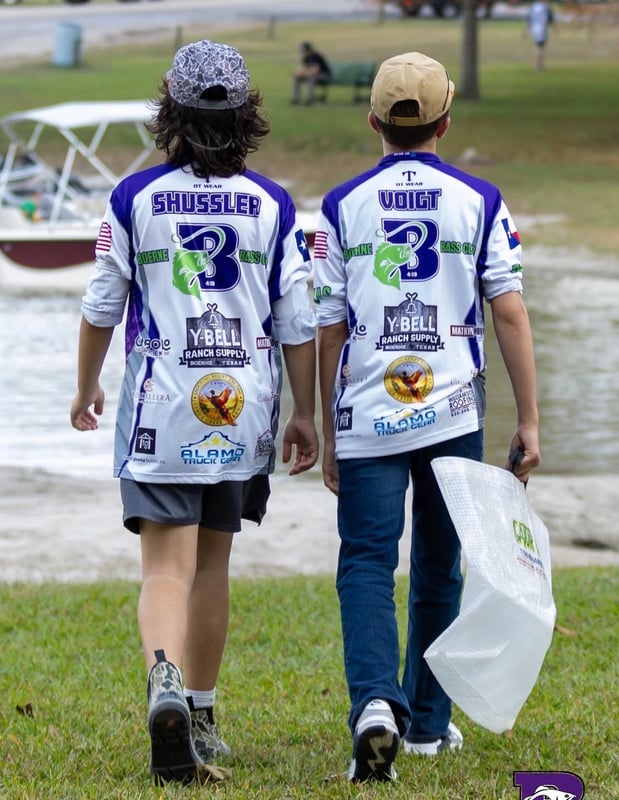 Two young anglers walking towards the water in tournament gear.