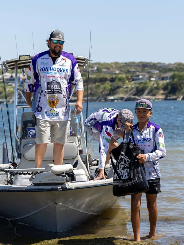 Young anglers at a bass fishing tournament by the shore.