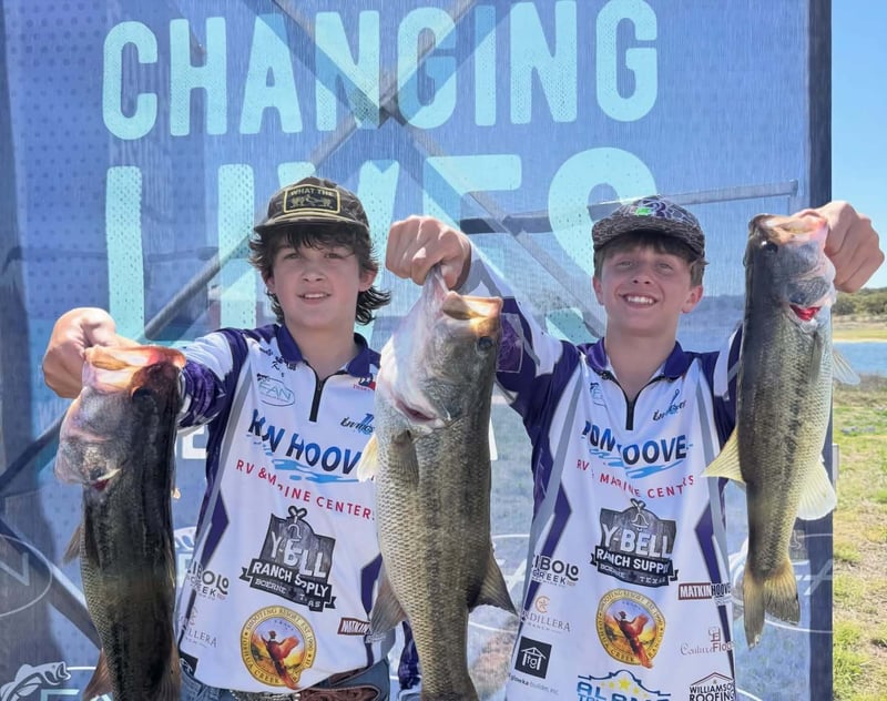 Two young anglers proudly holding their bass catches during a tournament.