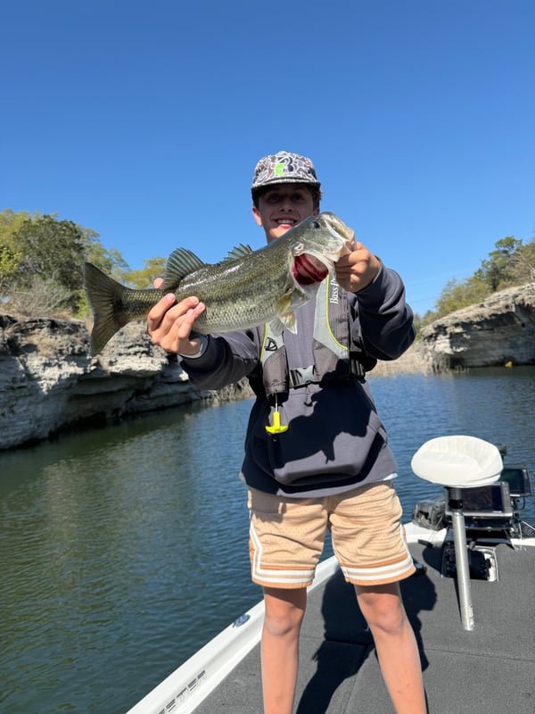 Young angler proudly holding a bass fish on a boat