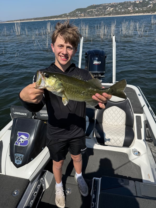 Young angler proudly holding a large bass catch on a boat