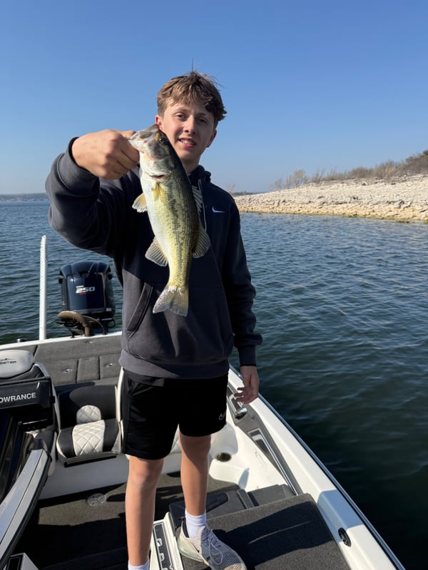 Young angler holding a caught bass on a fishing boat