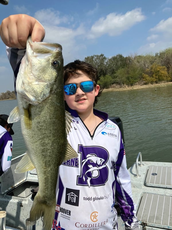 A young fisherman proudly holding a large bass caught during a tournament.