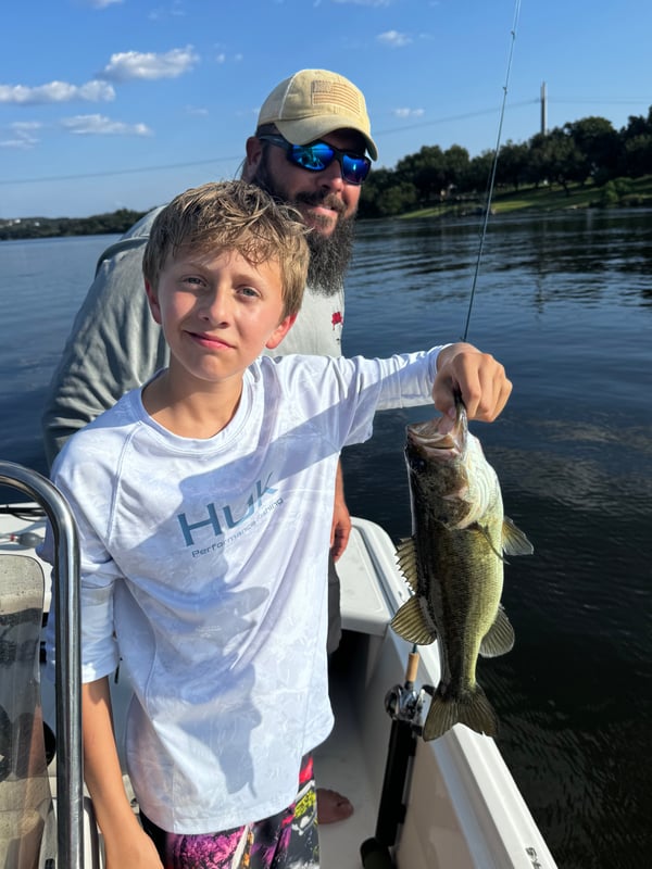 Young angler proudly holding a bass catch on a boat