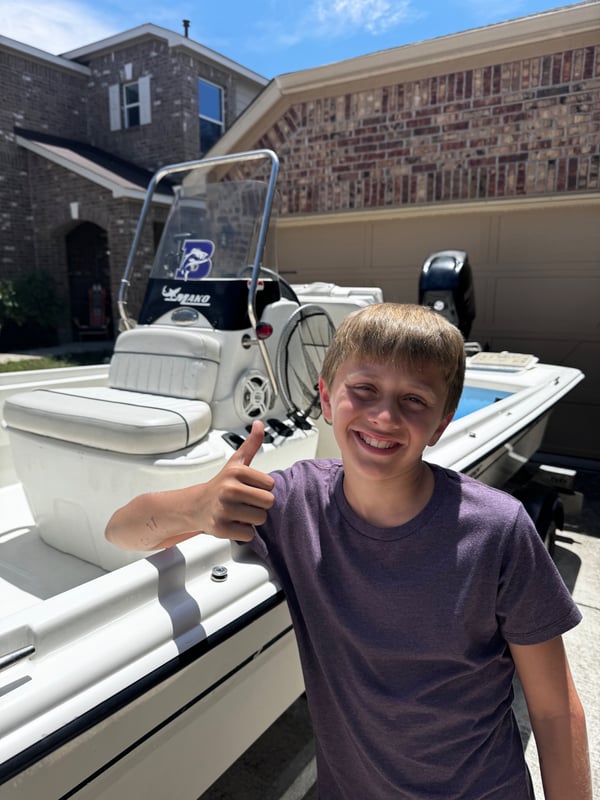 Youth angler giving a thumbs up by a fishing boat