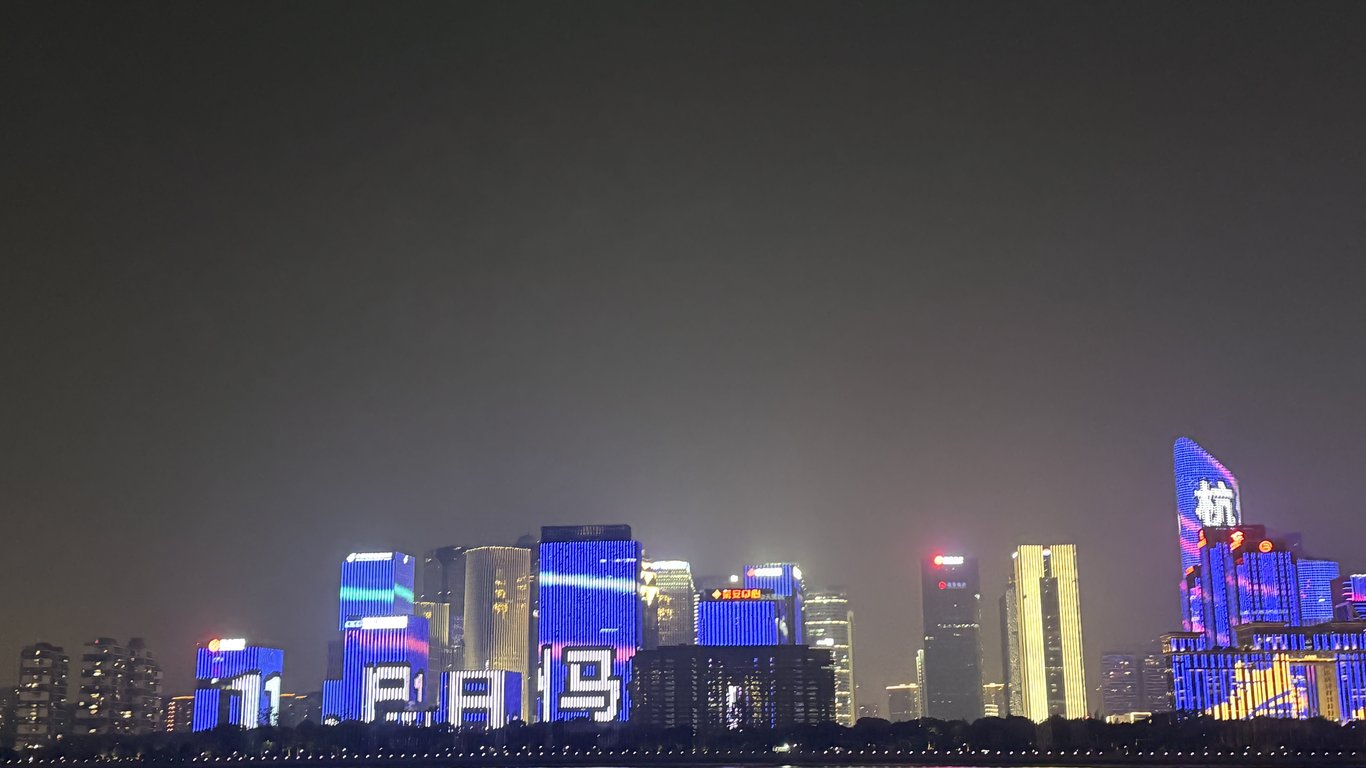 The Hangzhou riverside at night, the towers lit up as one screen.