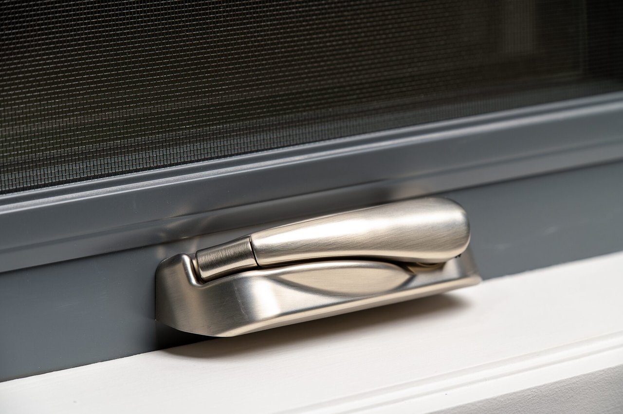 Close-up photograph of the rounded folding crank handle against a dark casement frame and insect screen