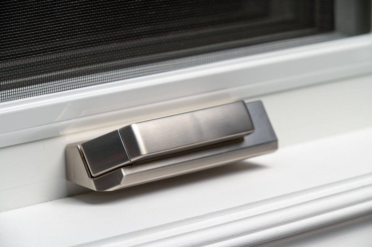 Close-up photograph of the straight folding crank handle against a white casement frame and insect screen