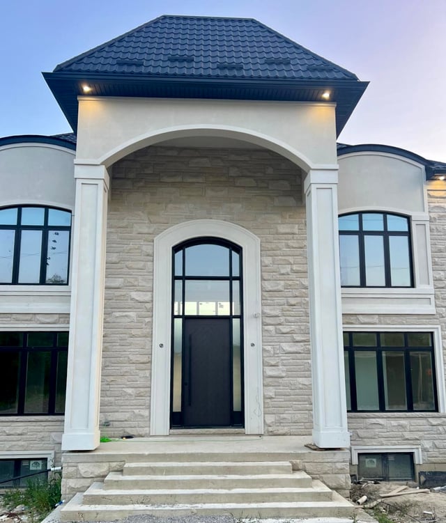 Dark entry door with tall sidelites and arched upper glazing beneath a covered stone entrance