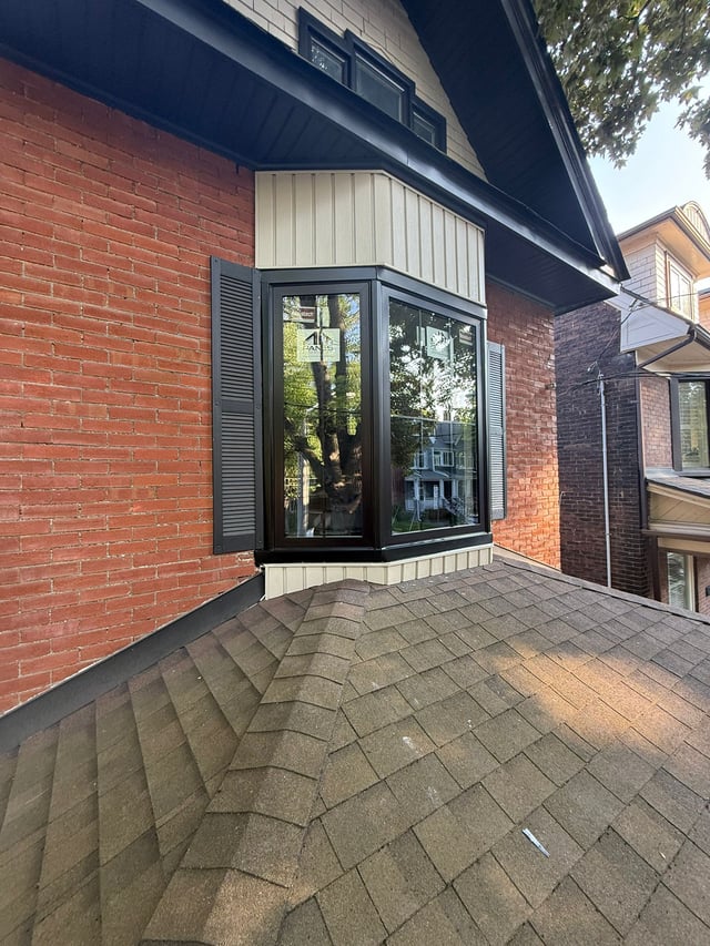 Dark-framed bay window projecting from a red-brick wall above a paved walkway