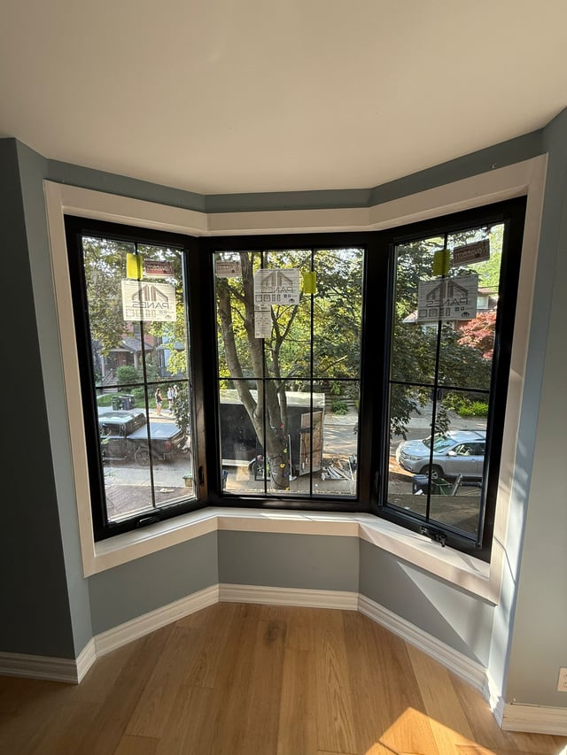 Interior of a dark-framed bay window with a white ledge above a wood floor