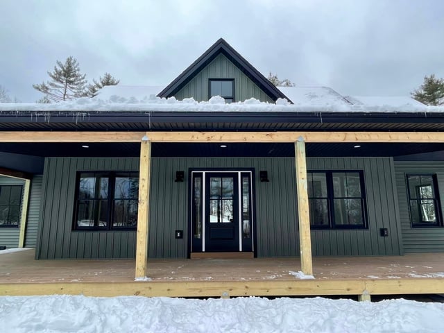 Dark-framed windows and a glazed entrance beneath a covered porch on a green-sided home