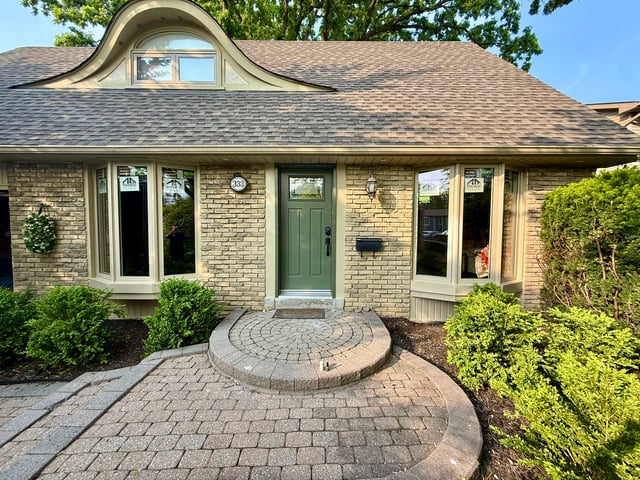 Green entry door between two white bay windows on a stone-fronted home