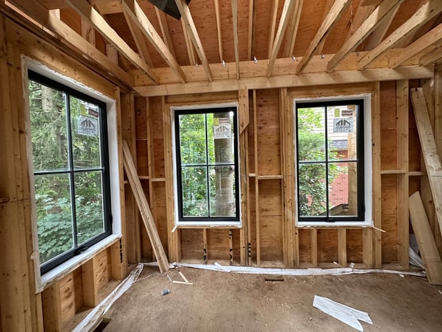 Three white windows with rectangular grids inside an unfinished timber-framed room