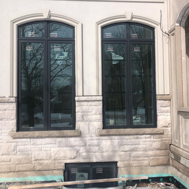 Two tall dark-framed window assemblies with arched tops in a light stone wall