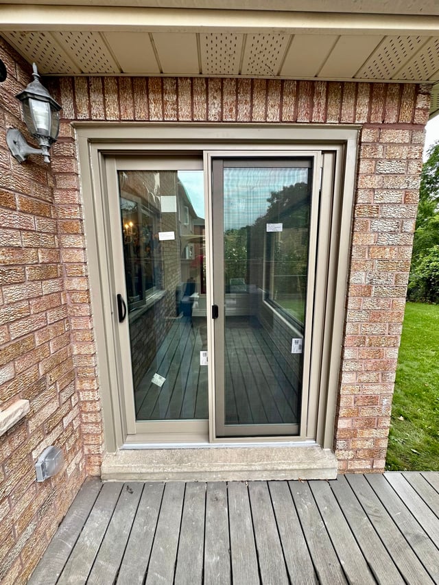 Tan two-panel sliding patio door between a brick wall and timber deck