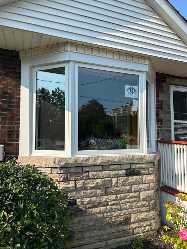 White bay window projecting from a brick and stone wall