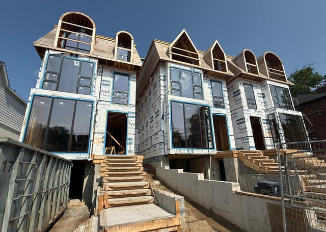Windows fitted into several openings of townhouses during construction, with wrapping and unfinished framing visible