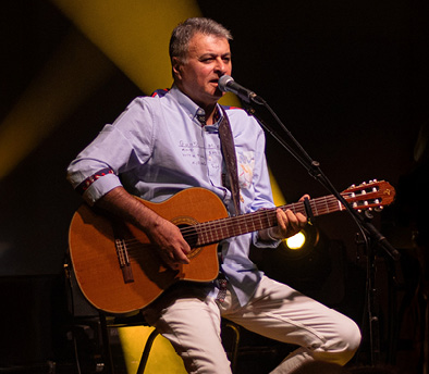 משה להב יושב על כיסא , מול מיקרופון , מנגן בגיטרה