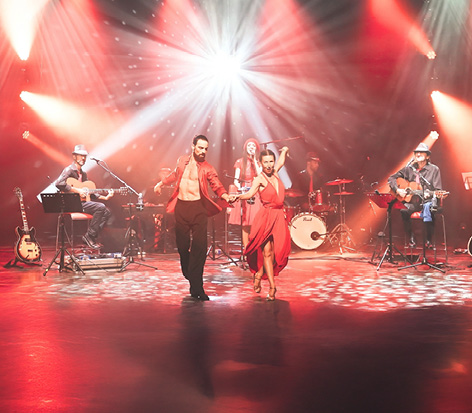 תמונה של 2 שחקנים רוקדים. ברקע להקה מנגנת בכלי נגינה שונים