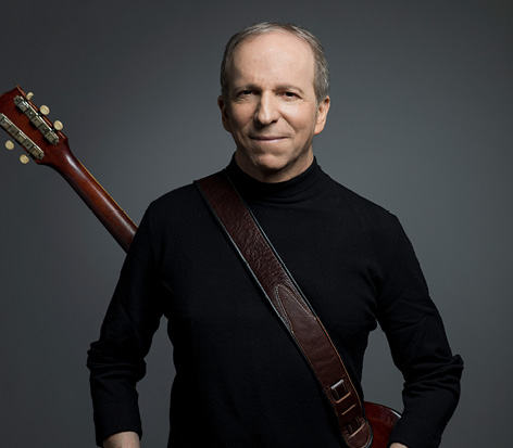 תמונה של דני סנדרסון מחייך עם גיטרה על הגב