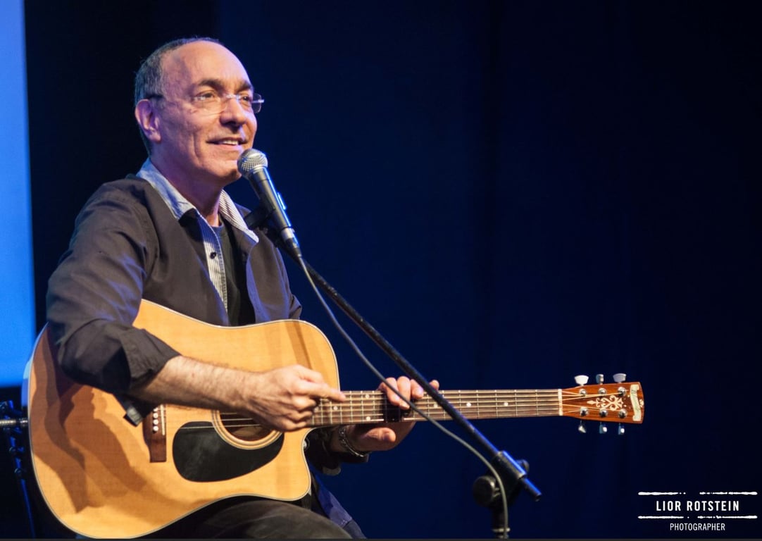 יובל דור מחזיק גיטרה מסתכל קדימה ומולו סטנד עם מיקרופון