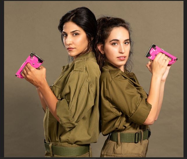 תמונה של מגי אזרזר ומשי קלינשטיין במדי צהל עומדות גב אל גב מחזיקות אקדח סיכות