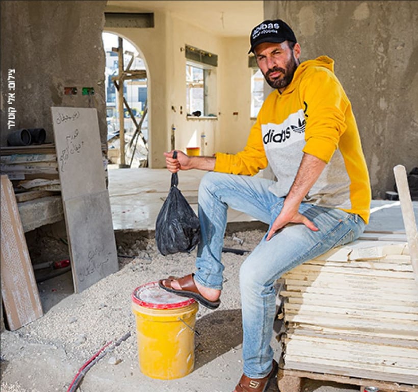 תמונה של אבו טבלה  יושב בתוך מבנה הרוס מחזיק שקית זבל